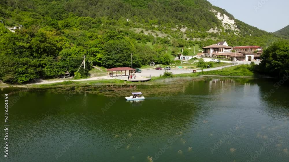 A cinematic flight over a mountain lake on which a catamaran is sailing. Summer water bike ride. Large mountains with white rocks are densely covered with green trees. Beautiful landscape. Summer trip A cinematic flight over a mountain lake on which a catamaran is sailing. Summer water bike ride. Large mountains with white rocks are densely covered with green trees. Beautiful landscape. Summer trip