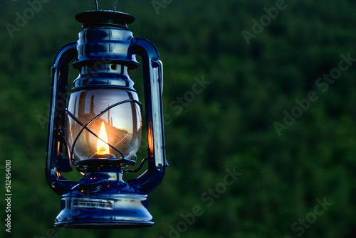 Kerosene lantern lamp with bright flame with green forest in the background © Vasil