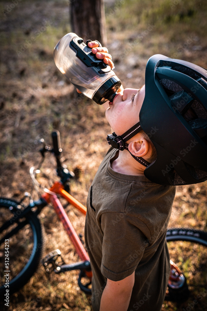 Naklejka premium a little boy with a bicycle behind drinks from a bottle
