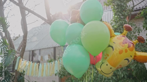 Backyard filled with green balloons and decoration for child birthday party. Green party decorations outside of a house. Giraffe balloon at sunny birthday party. High quality 4k footage