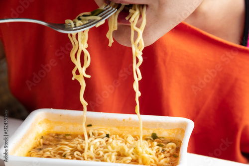 A woman eats instant noodles. Hot noodles on a fork.. White background. Noodles in the mouth and hanging into a plate. Noodles in the mouth and hanging into a plate