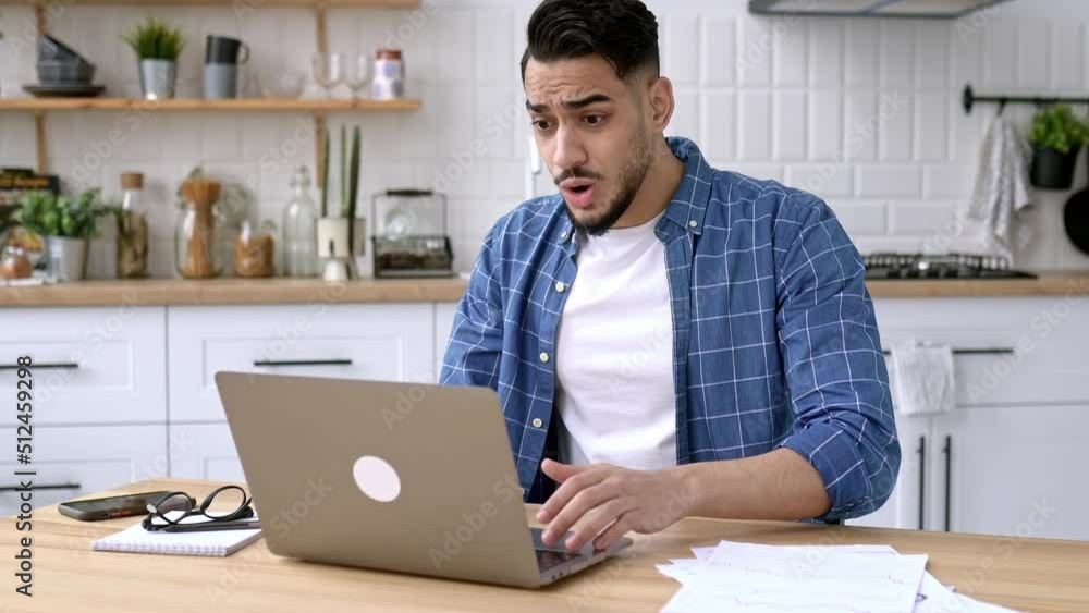 Angry stressed arabian or indian guy, sitting at desk in the kitchen, using laptop for online work, annoyed with bad result of his project, failed the deal, experiences negative emotions and stress Angry stressed arabian or indian guy, sitting at desk in the kitchen, using laptop for online work, annoyed with bad result of his project, failed the deal, experiences negative emotions and stress