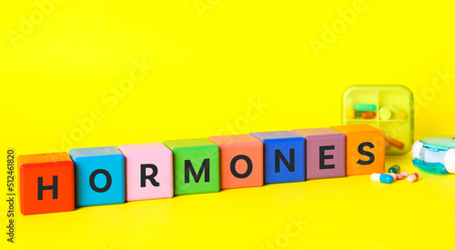 Word Hormones made of colorful cubes with letters and pills on yellow background