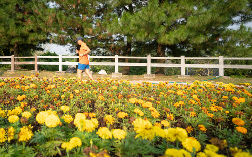Man runner jogging in a park with yellow blooming flowers at the foreground. Springtime or healthy lifestyle concept.