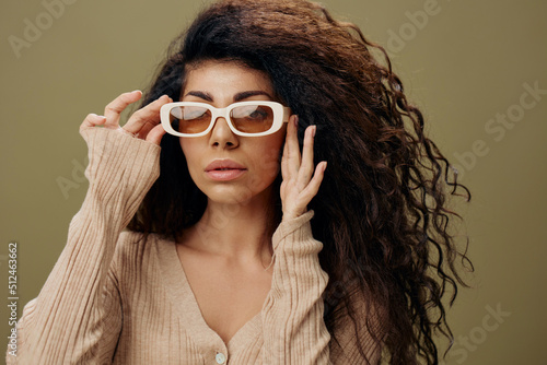 STYLISH EYEWEAR CONCEPT. Happy adorable tanned curly Latin female in casual things wear trendy sunglasses posing isolated over olive green background. Copy space Mockup Banner. Fashion closeup offer