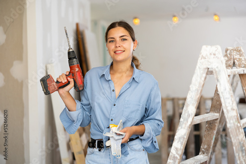 Portrait of smiling young woman with drill in apartment during renovation works.
