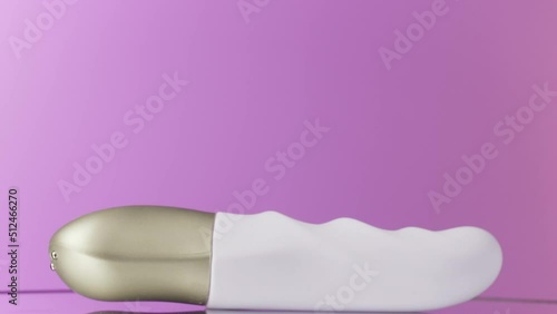 Bright purple background with white vibrator . Action . A compact massage device lying on a bright background that is filmed in close-up. photo