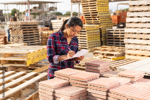 Photo Female worker with tablet checking quantity of paving slabs in warehouse of buil