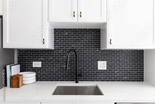Kitchen sink detail shot with white cabinets, small black marble subway tile backsplash, and a black faucet.