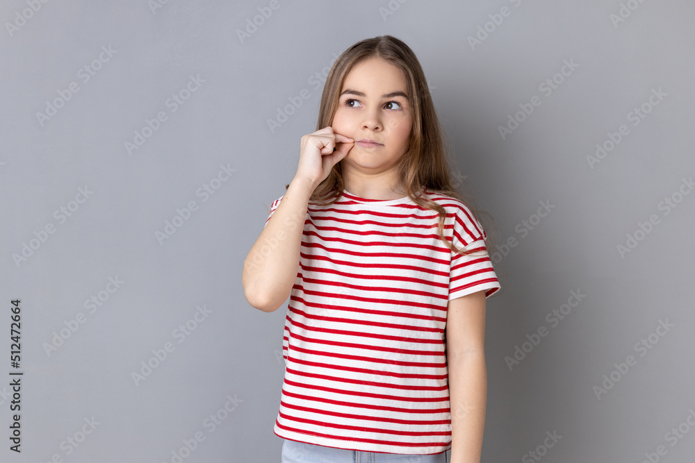 Portrait of adorable little girl wearing striped T-shirt having mystery look making zip gesture to close mouth, keeping secret, zipping lips. Indoor studio shot isolated on gray background. Portrait of adorable little girl wearing striped T-shirt having mystery look making zip gesture to close mouth, keeping secret, zipping lips. Indoor studio shot isolated on gray background.