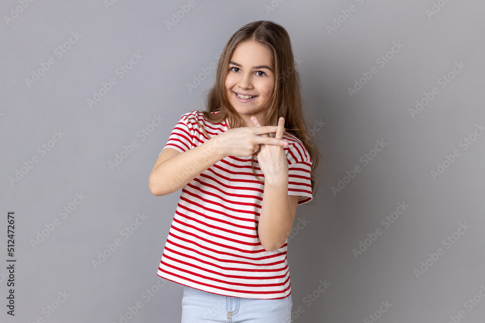 Internet trends. Portrait of little girl wearing striped T-shirt crossing fingers to make hashtag sign and looking at camera with toothy smile. Indoor studio shot isolated on gray background. Internet trends. Portrait of little girl wearing striped T-shirt crossing fingers to make hashtag sign and looking at camera with toothy smile. Indoor studio shot isolated on gray background.