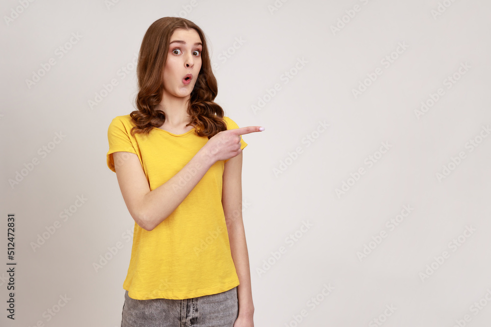 Portrait of amazed speechless pretty teenage girl collage student, standing with drop jaw and wondered, pointing at fascinating product. Indoor studio shot isolated on gray background. Portrait of amazed speechless pretty teenage girl collage student, standing with drop jaw and wondered, pointing at fascinating product. Indoor studio shot isolated on gray background.
