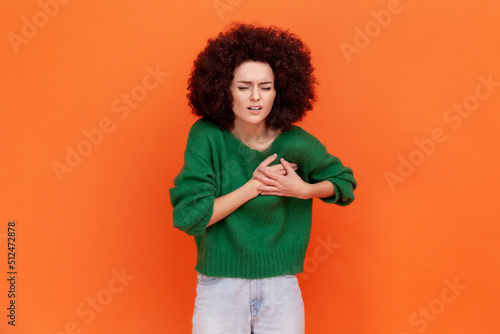 Fotografie, Obraz Portrait of ill woman with Afro hairstyle wearing green casual style sweater having hear attack, frowning from strong pain, needs hospitalization
