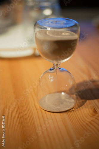Picture of an hourglass glass bottle on an empty wooden table.