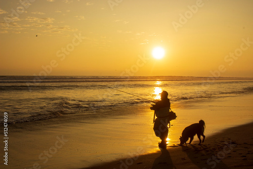 fisherman with his dog on the beach at sunset