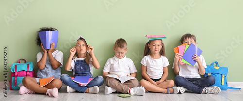 Funny little children with copybooks sitting on floor near green wall
