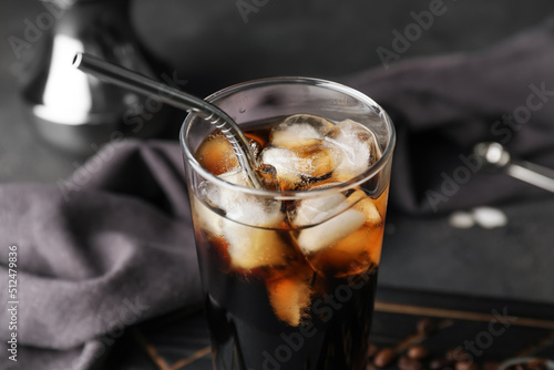 Glass with cold brew coffee and metal straw on dark background, closeup photo