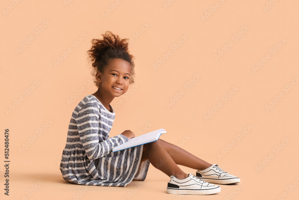 Little African-American girl reading book on beige background Little African-American girl reading book on beige background