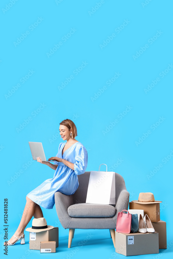 Young woman with laptop and new clothes on blue background. Online shopping Young woman with laptop and new clothes on blue background. Online shopping