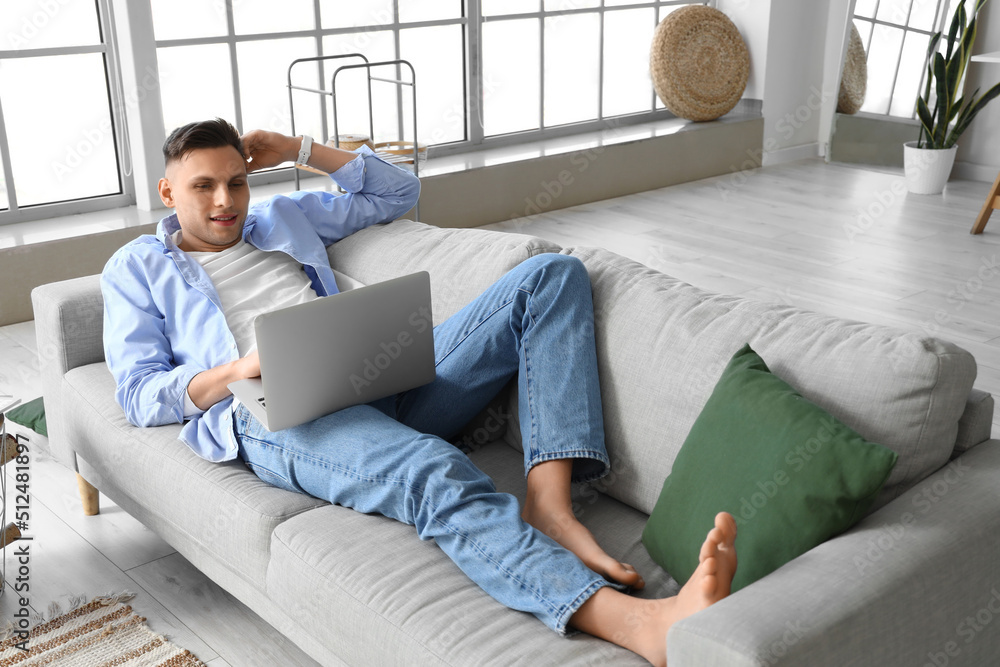 Young barefoot man using laptop on sofa at home Young barefoot man using laptop on sofa at home