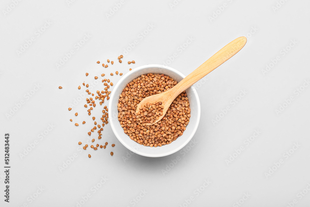 Bowl and wooden spoon with buckwheat grains on light background Bowl and wooden spoon with buckwheat grains on light background