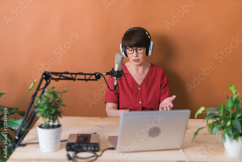 Middle-aged female radio presenter talking into the microphone and reading news - radio broadcast online concept photo