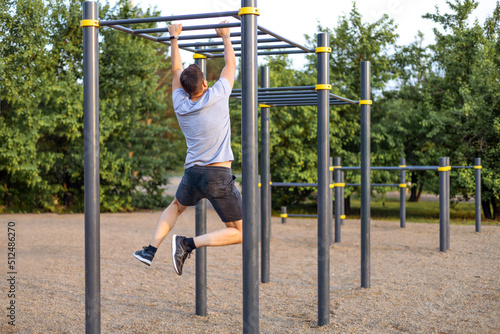 A man trains in an open area and pulls himself up on a horizontal bar. Outdoor fitness gym