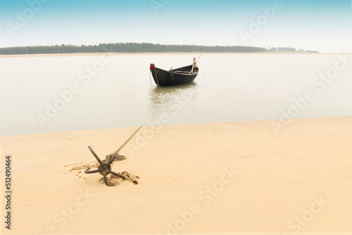 Moody image of a boat on water tied by a rope with an anchor on river bed at Tajpur, West Bengal, India. Minimalistic image. photo