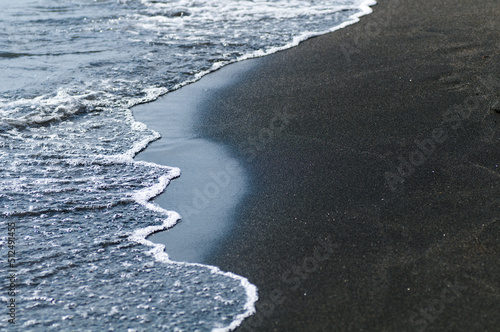Black volcanic magnetic sand on the seashore. Background texture of the beach with waves closeup. 