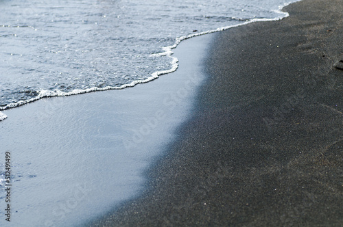 Black volcanic magnetic sand on the seashore. Background texture of the beach with waves closeup. 