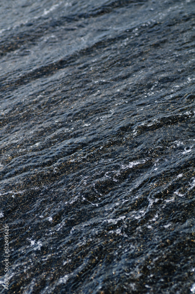 Black volcanic magnetic sand on the seashore. Background texture of the beach with waves closeup. 
