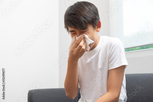 Sick Asian preteen boy blowing nose and sneeze at home, healthcare concept.