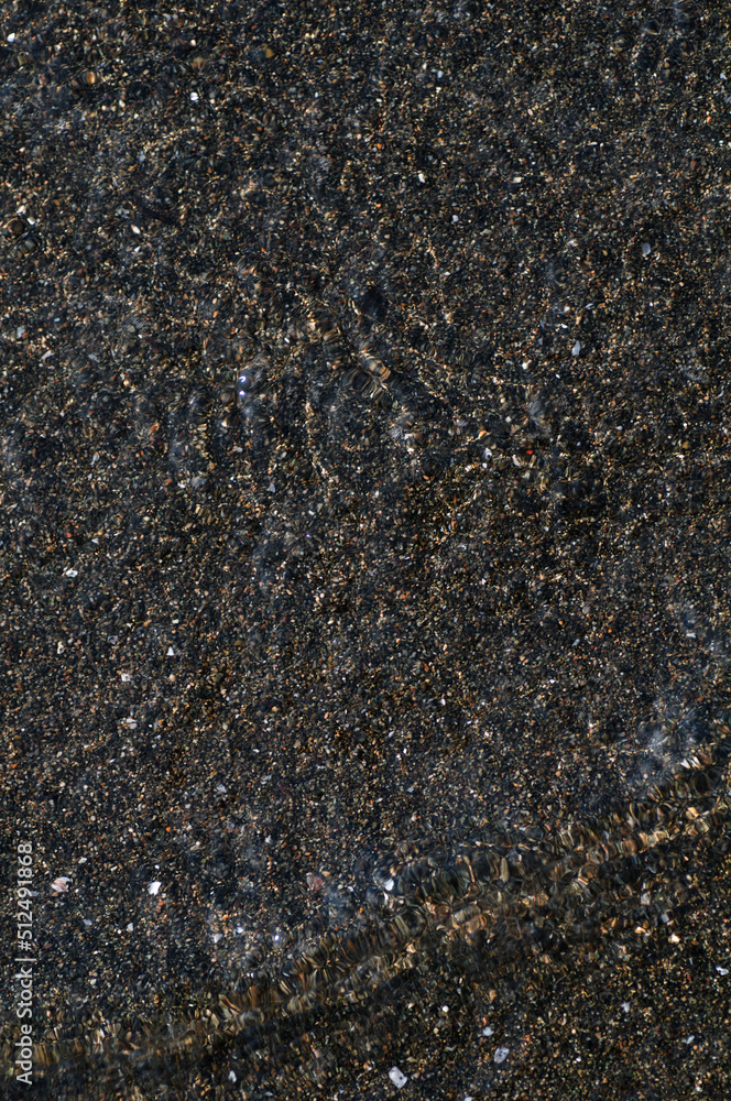 Black volcanic magnetic sand on the seashore. Background texture of the beach with waves closeup.
Black volcanic magnetic sand on the seashore. Background texture of the beach with waves closeup.