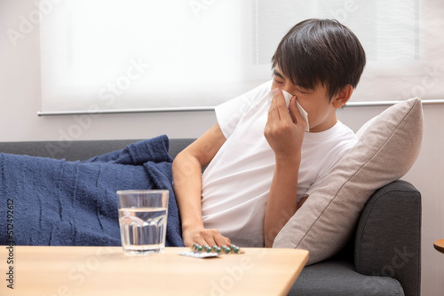 Sick Asian preteen boy coughing lying on sofa at home, healthcare concept.