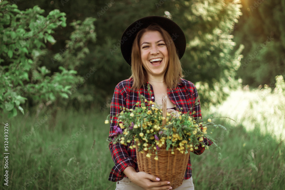 Summer lifestyle portrait of a beautiful young woman in a hat, smiling and holding a basket with a bouquet of wild flowers. The concept of happiness and love Summer lifestyle portrait of a beautiful young woman in a hat, smiling and holding a basket with a bouquet of wild flowers. The concept of happiness and love