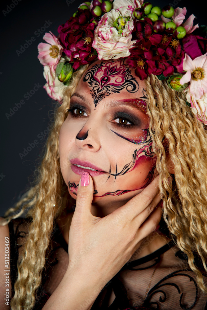 Naklejka premium Beautiful Halloween Make-Up Style. Blond curly hair Model Wear Sugar Skull Makeup with Red Roses. Santa Muerte concept. Model on black background in studio with wreath