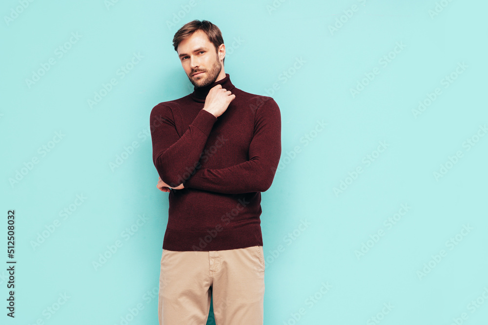 Portrait of handsome thoughtful stylish hipster lambersexual model. Sexy man dressed in turtleneck sweater and trousers. Fashion male isolated on blue wall in studio. Portrait of handsome thoughtful stylish hipster lambersexual model. Sexy man dressed in turtleneck sweater and trousers. Fashion male isolated on blue wall in studio.