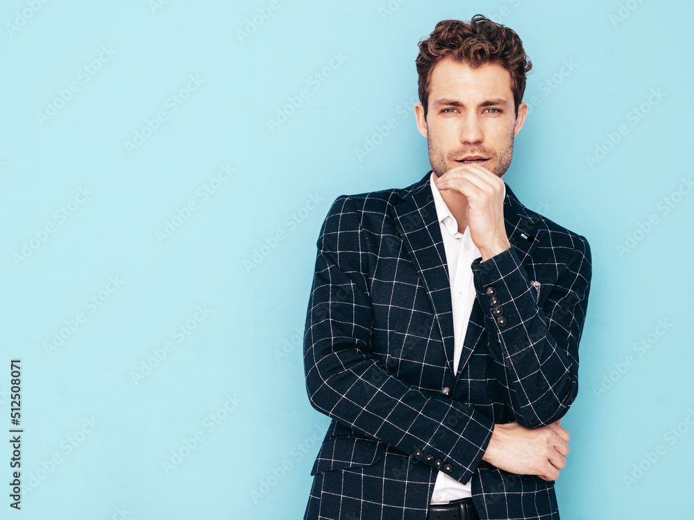 Obraz premium Closeup portrait of handsome confident stylish hipster lambersexual model. Sexy modern man dressed in black elegant suit. Fashion male posing in studio blue wall