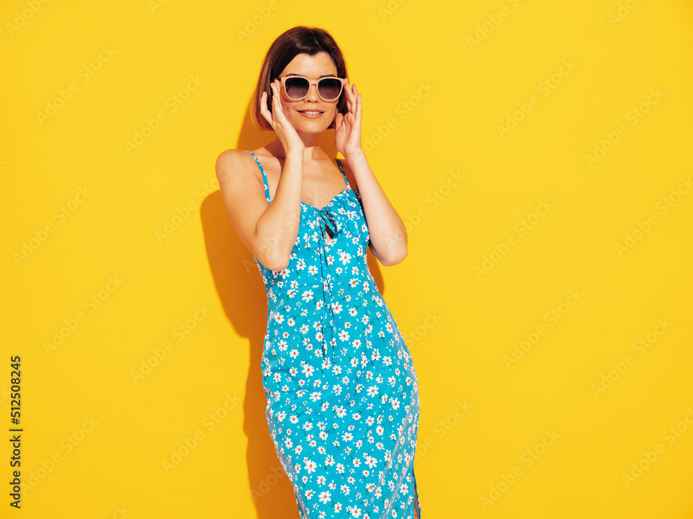 Young beautiful smiling female in trendy summer blue dress clothes. Carefree woman posing near yellow wall in studio. Sexy positive model having fun indoors. Cheerful and happy. In sunglasses Young beautiful smiling female in trendy summer blue dress clothes. Carefree woman posing near yellow wall in studio. Sexy positive model having fun indoors. Cheerful and happy. In sunglasses