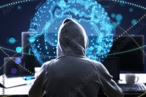 hacker at desktop using laptop with bright globe hologram. A holographic projection of planet earth. Flickering energy particles on blurry abstract dark background.  photo