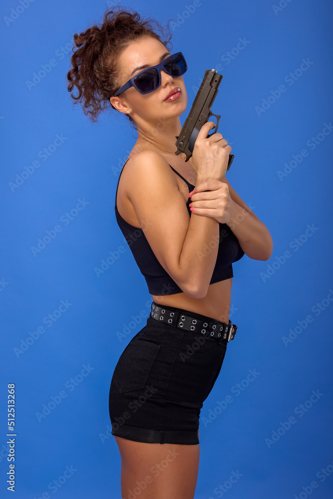 beautiful young woman with curly hair with a gun on a blue background beautiful young woman with curly hair with a gun on a blue background