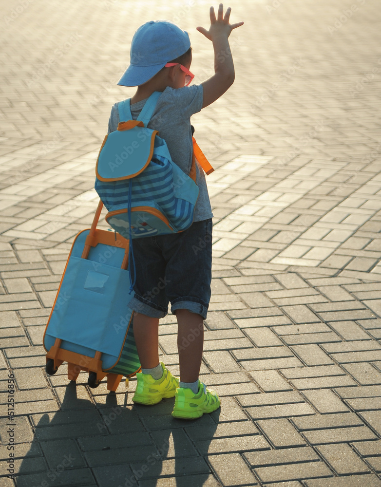 little boy with suitcase outdoors waiting for bus