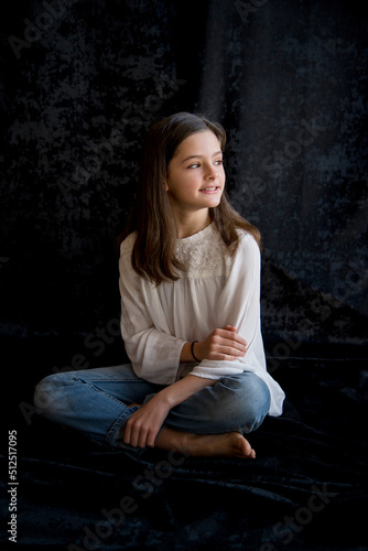 portrait of beautiful brunette girl sitting on a floor in blue jeans on black background