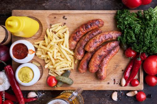 Tasty freshly grilled Sausages served with French fries and sauce on wooden board