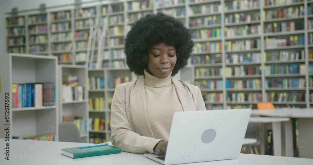 Young librarian works on laptop sitting at desk in library Young librarian works on laptop sitting at desk in library