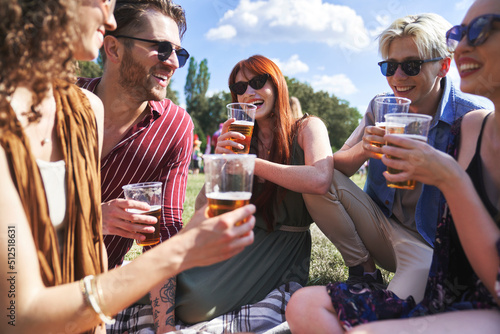 Group of young caucasian friends sitting on grass, drinking beer and having fun on music festival
