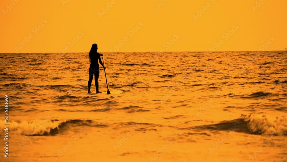 Woman In Silhouette Standing And Rowing On Paddleboard On Golden Ocean Woman In Silhouette Standing And Rowing On Paddleboard On Golden Ocean