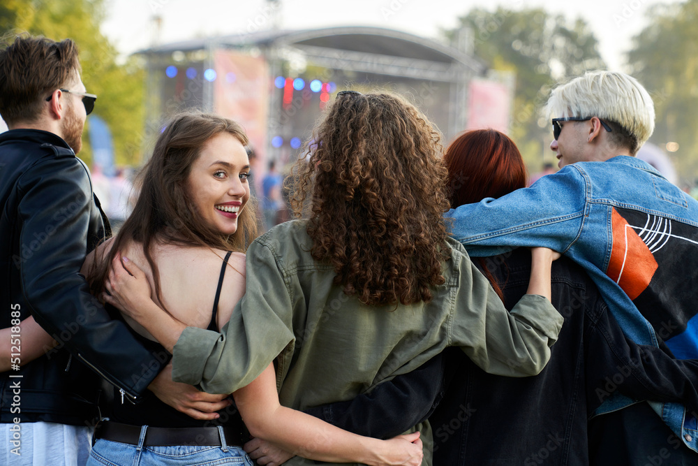 Fototapeta premium Group of young caucasian friends walking on music festival when one woman is turning toward camera