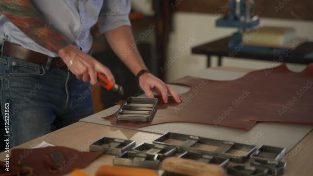 Leather craftsman works in his workshop. Master making leather products. Man carves leather sheet shape for die punch cutter leather punching knife. Male fits on craft cutting mold. Leather craftsman works in his workshop. Master making leather products. Man carves leather sheet shape for die punch cutter leather punching knife. Male fits on craft cutting mold.