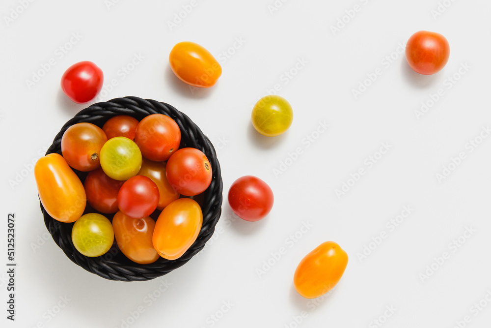 Cherry tomatoes in black basket on white background.